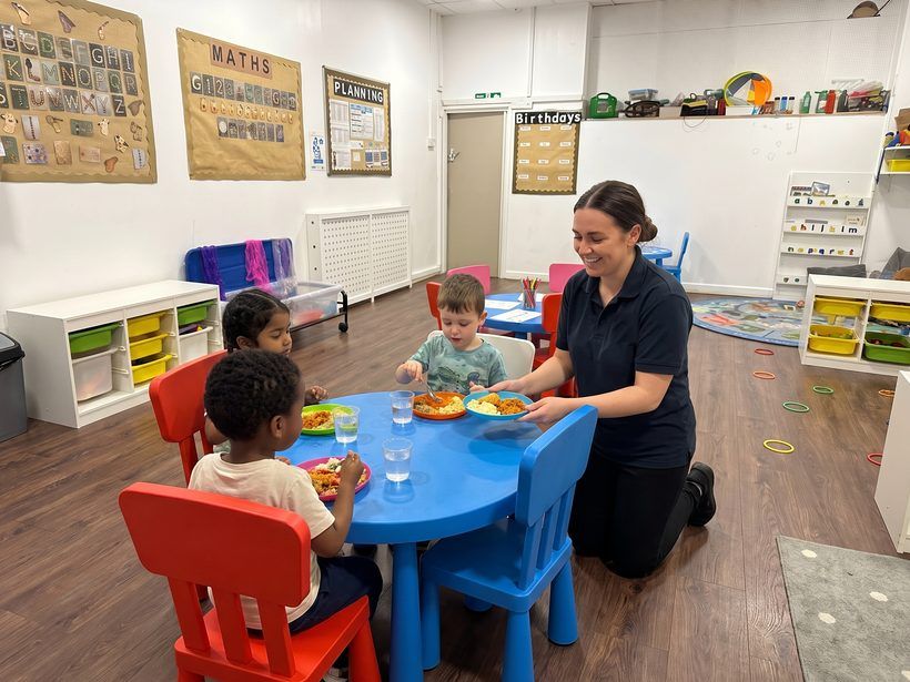 Mealtime at a low table in the Golden Kidz Daycare toddler room, beneath the maths and alphabet displays